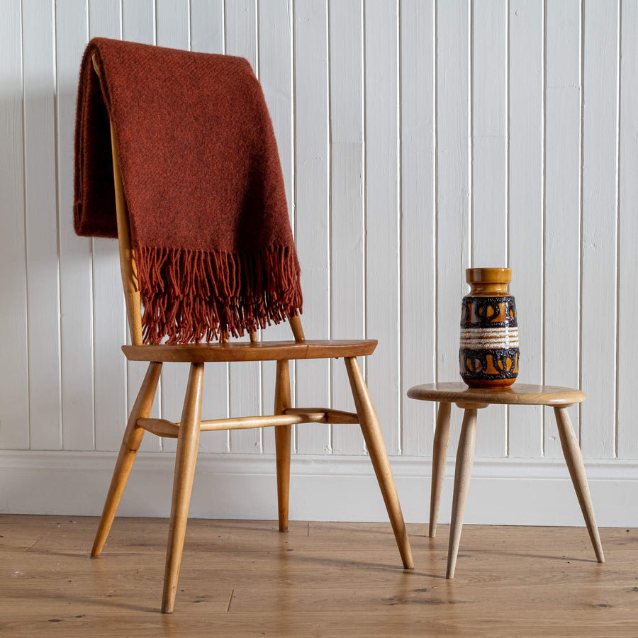 Gotland Wool Blanket – Rust, folded on the back of a chair with vintage vase